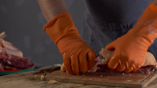 Male cook in orange gloves and gray apron chops turkey on a wooden board. Preparing for Thanksgiving.