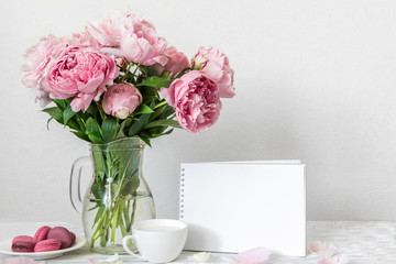 Still life with bouquet of pink peony flowers, blank greeting card, cup of cappuccino and macaroons. mock up