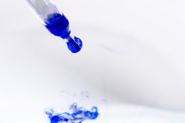 blue ink drips from a pipette into a light liquid