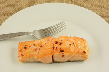 Baked salmon fish fillet with crushed red pepper glaze on white late with fork