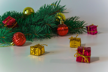 A photograph of a branch of a coniferous tree, near which toys for decorating the Christmas tree lie on a light background.