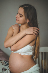 Naklejka premium Attractive pregnant woman is sitting in bed and holding her belly. Last months of pregnancy.