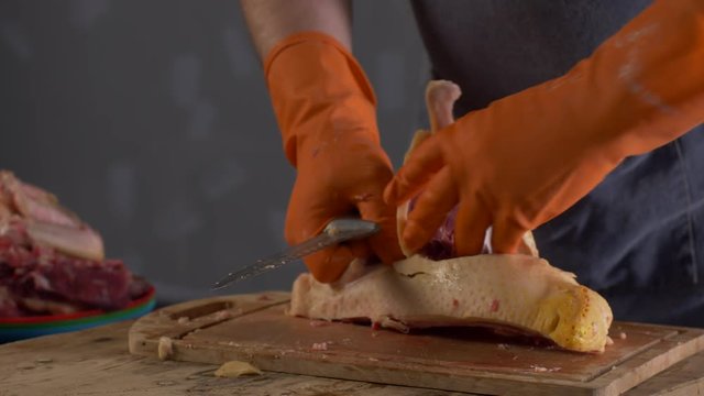 Male cook in orange gloves and gray apron chops turkey on a wooden board. Preparing for Thanksgiving.