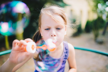 little girl blowing soap bubbles in summer park at playground