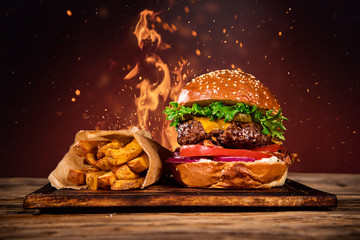 Tasty burger with french fries and fire. - obrazy, fototapety, plakaty