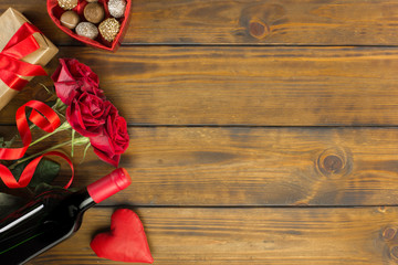 Valentines day romantic decoration with roses, wine and chocolate on a brown wooden table. Top view, copy space.