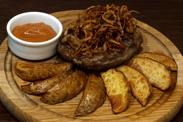  steak with fried onions, potatoes and sauce. On a wooden board close-up