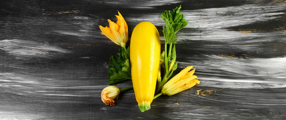Fresh yellow zucchini and zucchini flowers on a black wooden table. Top view. Copy space