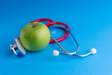 Green Apple with medical stethoscope isolated on blue background for healthy eating. Selective focus and crop fragment. Healthy, Diet and copy space concept