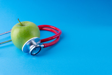 Green Apple with medical stethoscope isolated on blue background for healthy eating. Selective...