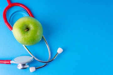 Green Apple with medical stethoscope isolated on blue background for healthy eating. Selective...