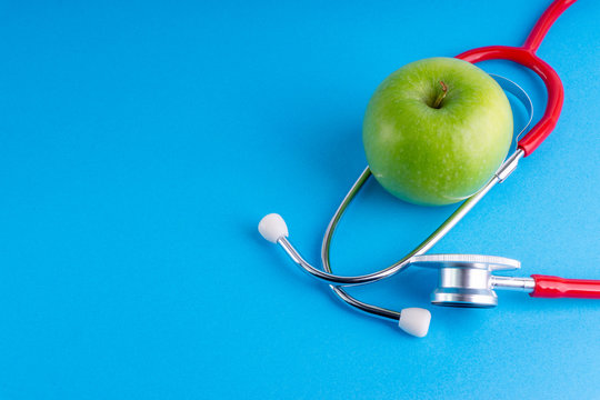 Green Apple with medical stethoscope isolated on blue background for healthy eating. Selective focus and crop fragment. Healthy, Diet and copy space concept