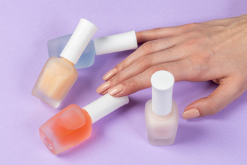 Female's hand holding bottles with colorful nail polish of purple background