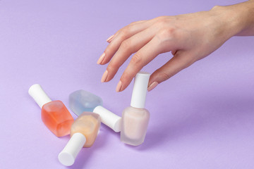 Female's hand holding bottles with colorful nail polish of purple background