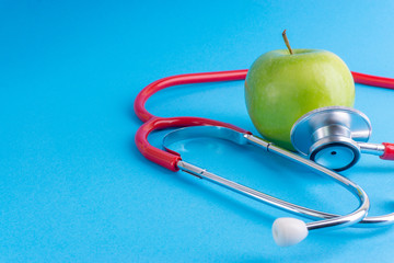 Green Apple with medical stethoscope isolated on blue background for healthy eating. Selective focus and crop fragment. Healthy, Diet and copy space concept