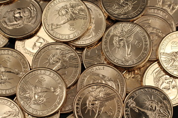 A close up image of a pile of American one dollar coins on a clean, black background