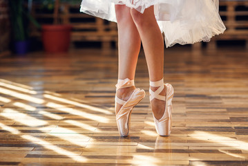 Close-up dancing legs of ballerina wearing white pointe ballet shoes in the dancing hall.