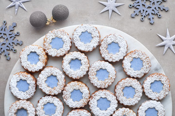 Top view of flower Linzer cookies with blue glazing on white marble serving board with winter decorations