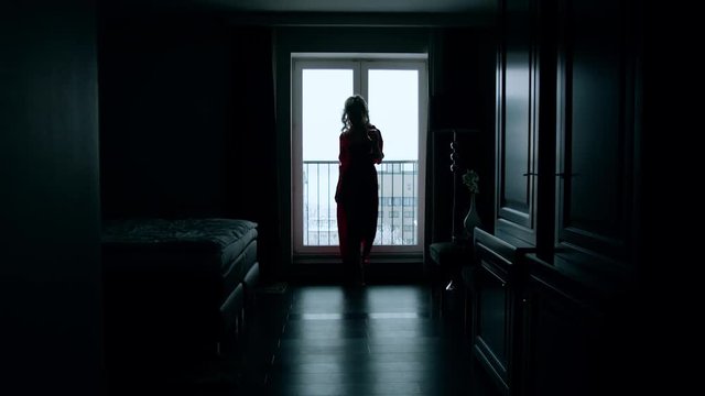 Silhouette of a woman with great body walking forward slowly taking off her robe. Luxury hotel room, balcony on a background. Shoot with RED RAVEN camera.