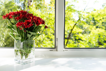 The window is a glass vase with red chrysanthemums.