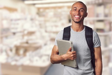 Smiling African Student man with laptop, mall background, bokeh