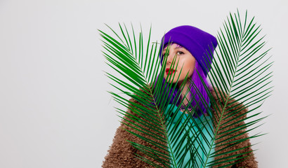 Beautiful young girl with purple hair in jacket with palm leaf on white background.