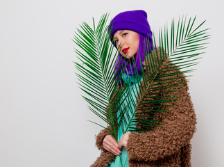 Beautiful young girl with purple hair in jacket with palm leaf on white background.