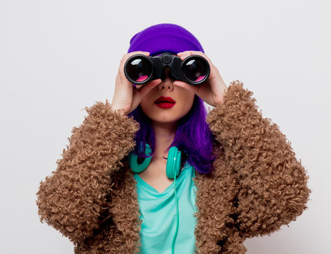 Beautiful young girl with purple hair in jacket looking in to binocular on white background.