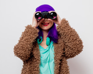 Beautiful young girl with purple hair in jacket looking in to binocular on white background.