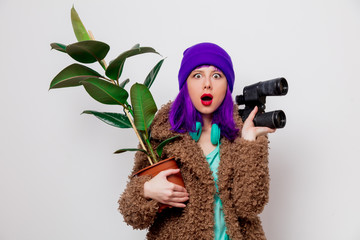 Beautiful young girl with purple hair in jacket with binocular and plant on white background.