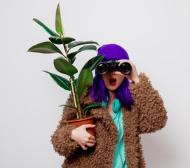 Beautiful young girl with purple hair in jacket with binocular and plant on white background.