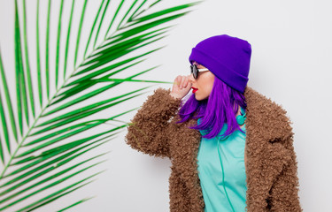 Beautiful young girl with purple hair in jacket with palm leaf on white background.