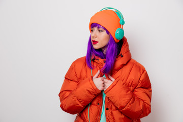 Beautiful young girl with purple hair and in orange jacket listen music in headphones on white...