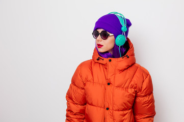 Beautiful young girl with purple hair and in orange jacket listen music in headphones on white background.