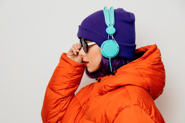 Beautiful young girl with purple hair and in orange jacket listen music in headphones on white background.