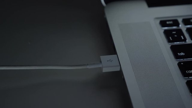 Close-up shot of male hand fastly inserting usb cable into laptop on black table background.