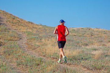 rear view of athletic runner running on a mountain trail on a blue sky background