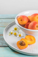 Obraz na płótnie Canvas Delicious ripe apricots in a bowl on the wooden table. Close-up with apricots and daisy flowers