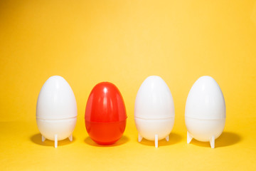 Difference concept. Four eggs on yellow. One red and three white plastic eggs