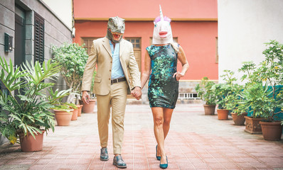 Crazy senior couple wearing dinosaur and unicorn mask - Mature trendy people having fun masked at carnival parade - Absurd, eccentric, surreal, fest and funny masquerade concept © Alessandro Biascioli