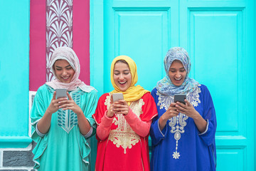 Happy muslim women using their mobile smart phones in the college - Arabian young people watching on cellphone and laughing together outdoor - Millennials, generation z and technology concept