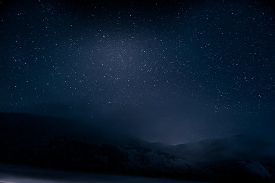 Beautiful blue dark night sky with many stars above snowy mountains