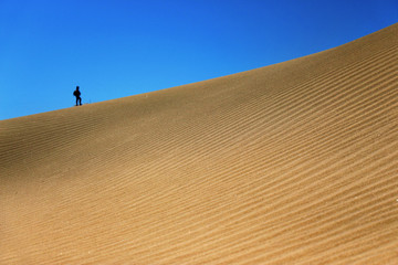 A minimalism of Maspalomas sand dunes in Gran Canaria. A tiny man in the background gives a create scale how huge the sand dunes are.