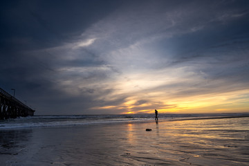 Silhouetted fisherman and pier on a sunset beach with reflections