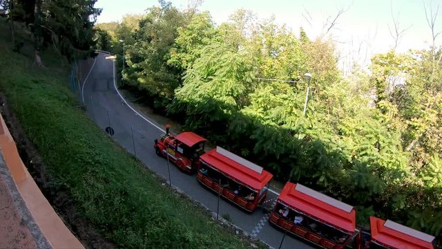 Little touristic train to San Luca church on Bologna hill. Departing from city downtown up to the sanctuary on the Colle della Guardia hill. Bologna city of Italy. Aerial view beside porch stairway.