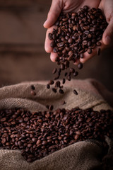Crop close-up view of hands with coffee beans pouring to sack