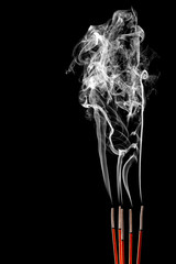 Closeup of calmly burning incense sticks with fume on black background