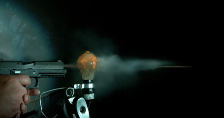 Gun shooting a bullet through a light bulb and exploding it into a million pieces, moment of impact, 