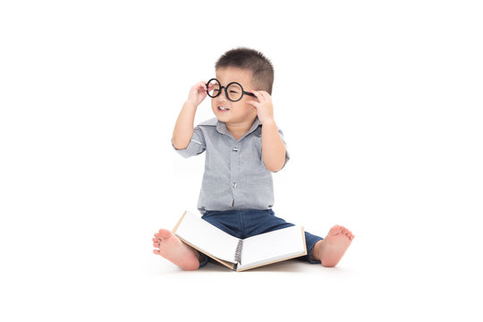 Cute little child play with book and wearing glasses while sitting on floor isolated over white background, Asian baby boy and education concept