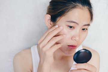 Portrait of Asian woman worry about her face when she saw the problem of acne and scar by the mini...